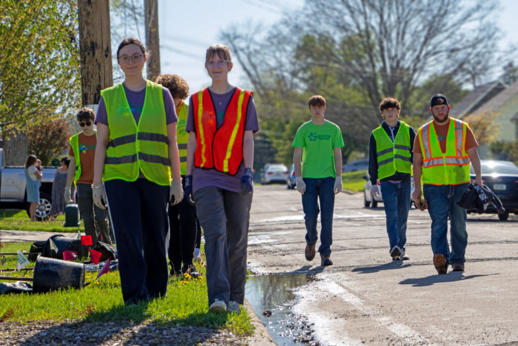 Teenage volunteers in safety vests walking along a roadside during a community cleanup.