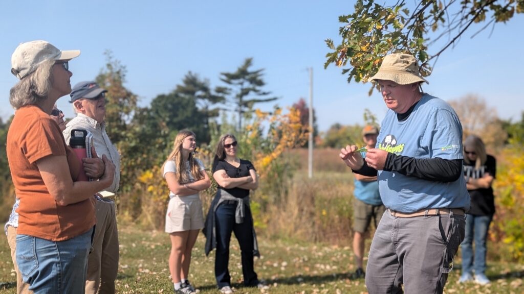 An instructor holding an oak branch, showing the leaves to a small group standing outdoors.