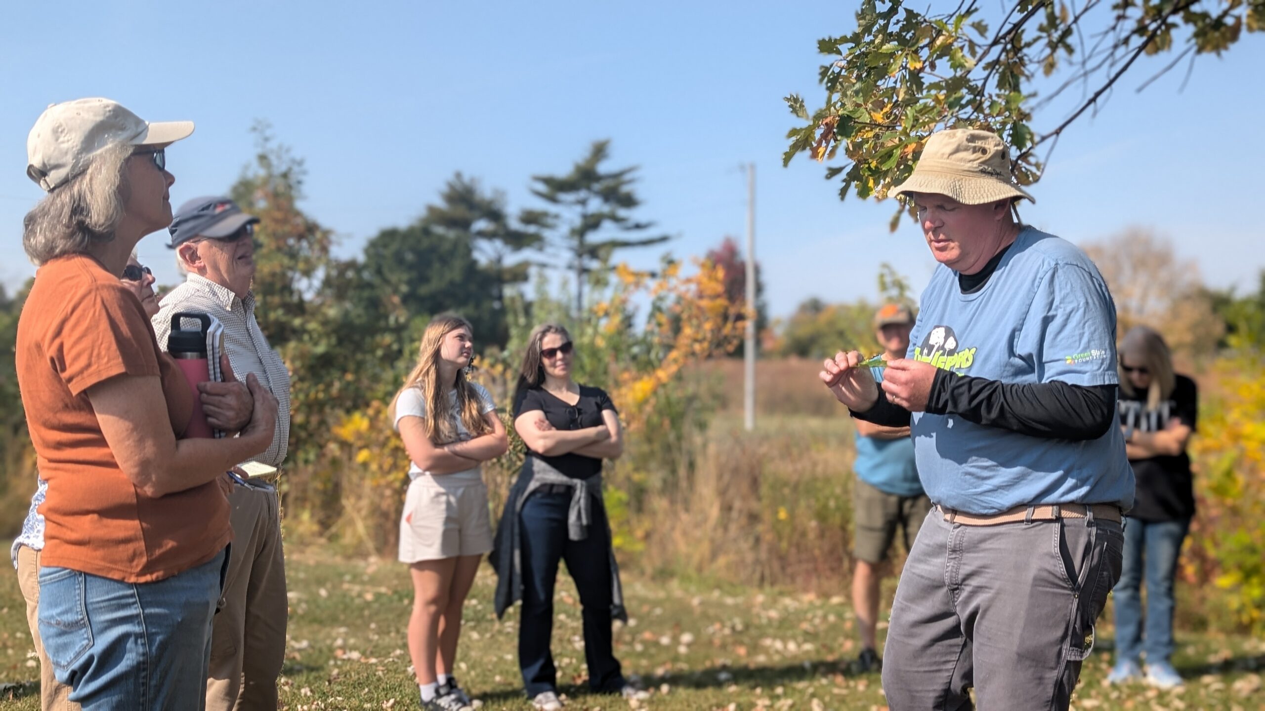 An instructor holding an oak branch, showing the leaves to a small group standing outdoors.